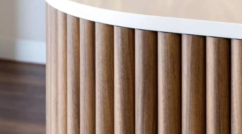 Una base de isla de cocina curvada con listones verticales de madera, rematada por una encimera blanca y lisa. | DOMUS Acabados